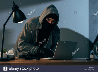 burglar-in-mask-and-gloves-typing-on-laptop-keyboard-in-dark-room-T22C9A.jpg