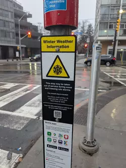 Sign next to a bus stop in Toronto stating that the stop is not in service during snowstorms and freezing rain storms
