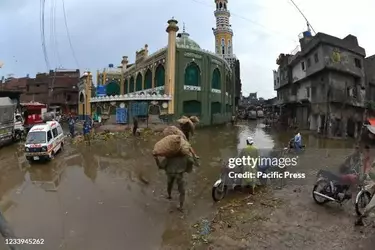 lahore-punjab-pakistan-pakistani-commuters-wade-through-a-flooded-street-after-heavy-monsoon-...webp