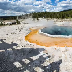 A steaming hot spring in Yellowstone National Park, glowing with vibrant blue, orange, and white mineral layers. In the foreground, shadows cast on the ground resemble iconic Star Wars characters from a galaxy far, far away.