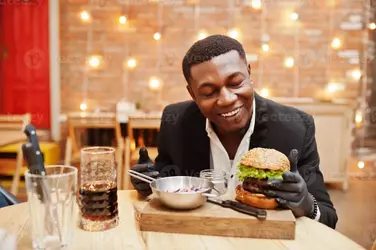respectable-young-african-american-man-in-black-suit-and-gloves-for-food-sitting-in-restauran...webp
